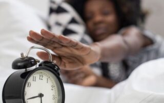 black woman waking up and turning off her alarm clock.