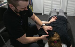 Male chiropractor performing soft tissue work on a female patient experiencing shoulder strain.