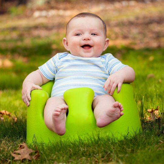 Baby sitting in green bumbo floor seat in the grass.