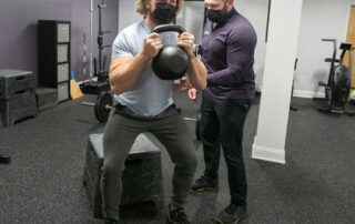 Male chiropractor taking male patient through a goblet box squat.