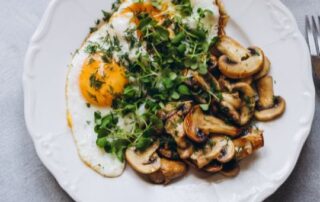 A white plate with eggs, mushrooms, potatoes, and microgreens.