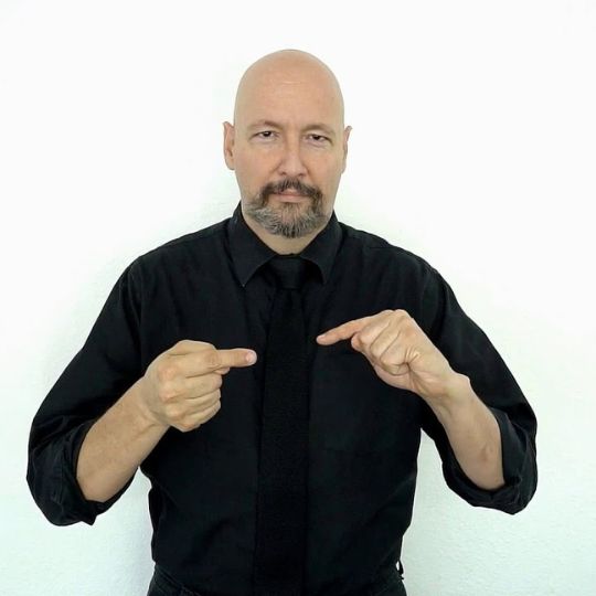 Bald caucasian man with mustache signing "pain" in American Sign Language.