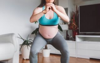 Pregnant woman performing an air squat in her living room.