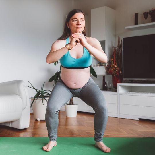 Pregnant woman performing an air squat in her living room.