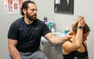 Male chiropractor assessing a female patient's neck pain.