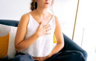 Caucasian woman with her one hand on her heart and one hand on her belly practicing breathwork.