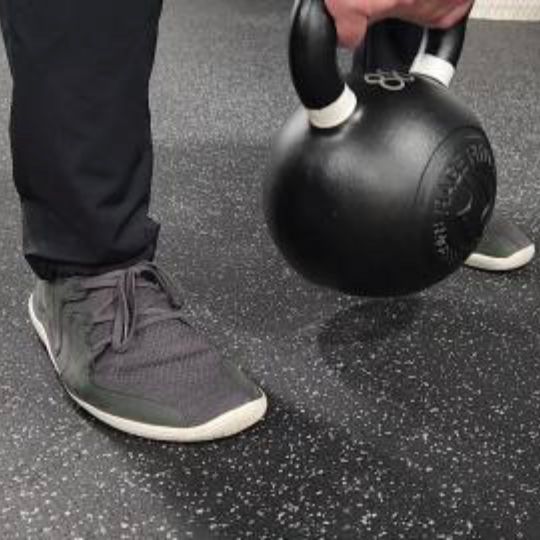 Man performing a kettle bell deadlift while wearing wide toe box shoes.