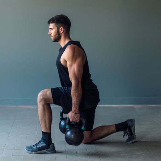 Caucasian man performing split squats with kettle bell weights.