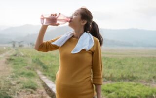 Pregnant woman drinking a bottle of water mid walk.