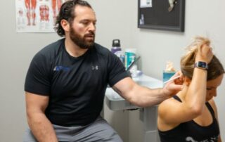 Male chiropractor assessing female patient's neck pain.