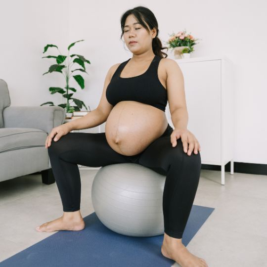Pregnant asian woman performing an exercise on a balance ball.