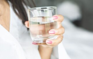 Caucasian woman with dark hair holding a glass of water.