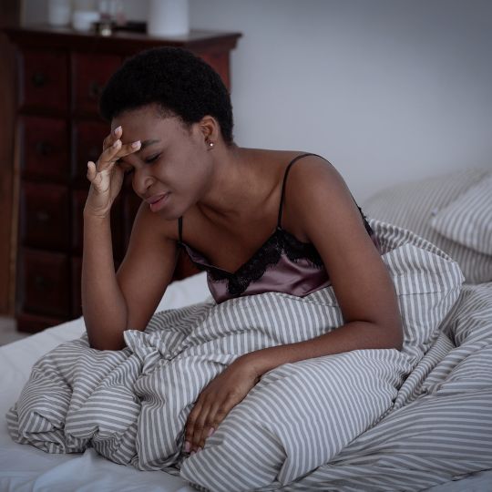 African American woman sitting in bed suffering from a migraine headache.