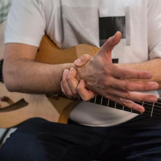 Caucasian man experiencing wrist pain while playing a guitar.