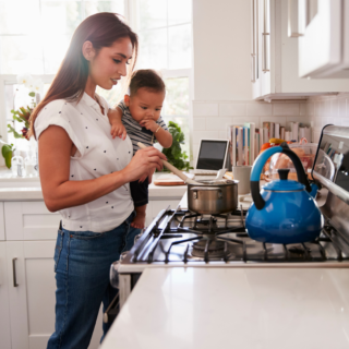 Mother cooking dinner while holding her baby.