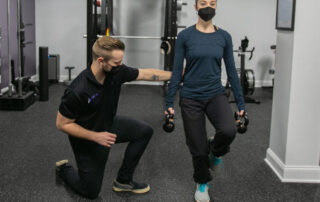 Male chiropractor monitoring dancer doing rehab exercises with kettlebells.