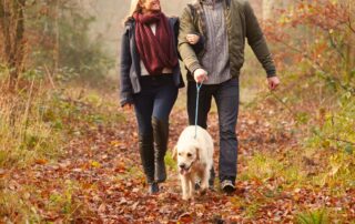 man and woman walking dog on a leaf covered trail.