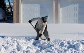 woman bundled up, shoveling her driveway