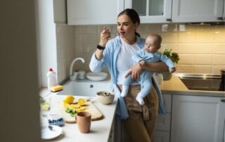 Young caucasian mom eating a meal while holding a baby.