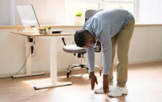 man in work attire stretching next to his desk.