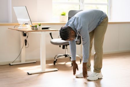 man in work attire stretching next to his desk.