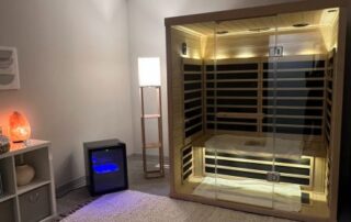 Infrared sauna with white light on. Room also includes a floor lamp, mini fridge with cold towels, and salt lamp.