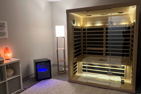 Infrared sauna with white light on. Room also includes a floor lamp, mini fridge with cold towels, and salt lamp.