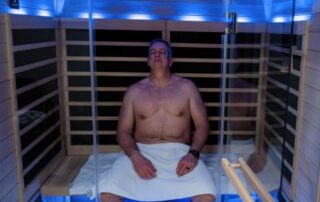 Caucasian male sitting in infrared sauna with blue light.