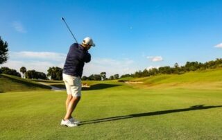 Golfer mid-swing on a sunny course, demonstrating strong posture and full-body movement.