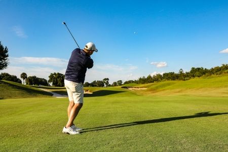 Golfer mid-swing on a sunny course, demonstrating strong posture and full-body movement.