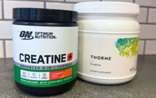 Two creatine supplement containers on a countertop—Optimum Nutrition’s strawberry peach flavored Creatine+ and Thorne’s unflavored creatine powder.