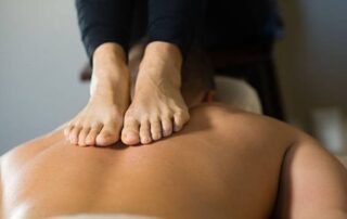 Massage therapist performing Ashiatsu using their feet to apply deep pressure to a client's back.