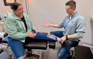 Male chiropractor demonstrating how to apply an ice pack to a patient’s ankle injury.